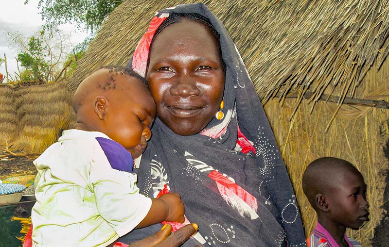 A mother holding her young child in her arms in front of a house