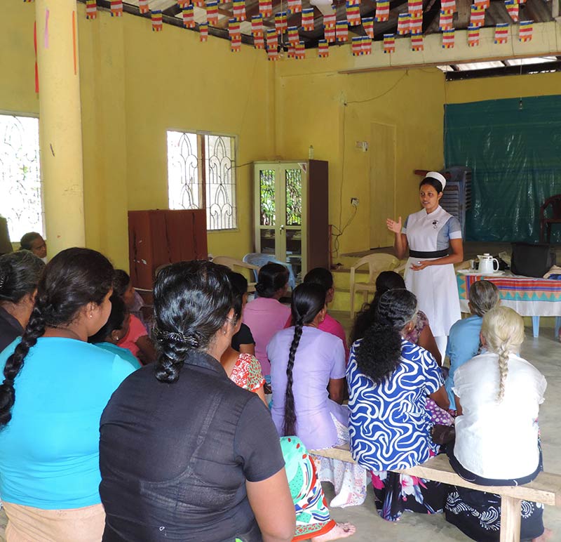 A female nurse tutor standing in front of a classroom of ladies sitting down on benches