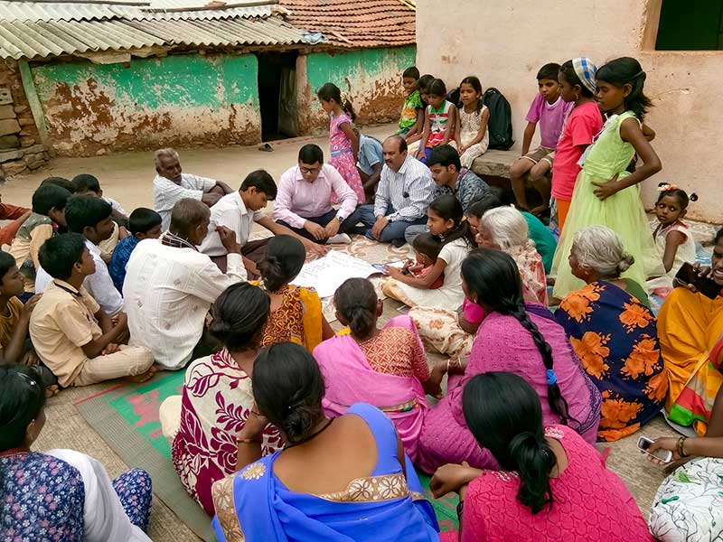 A group of men and women sitting together on mats outside.