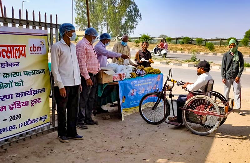 Five people standing at a desk outdoors handing items to a man in a disability vehicle