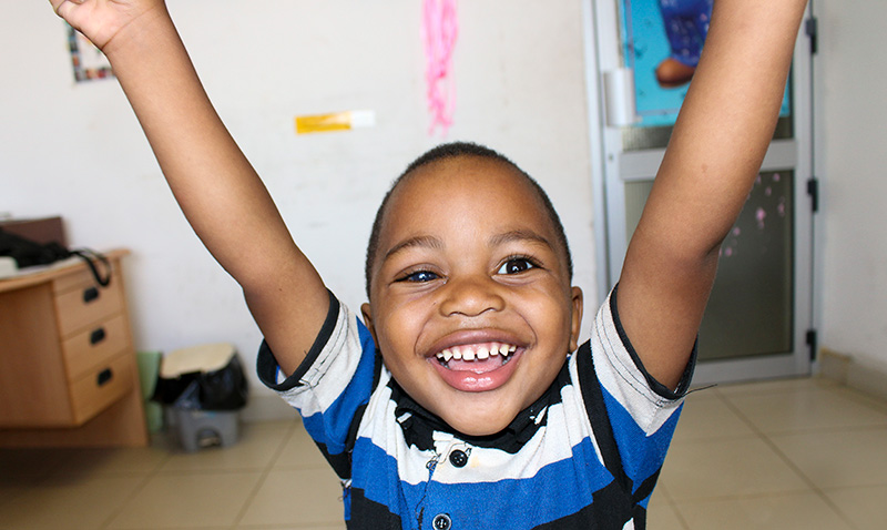 A young child smiling, holding their arms up in the air