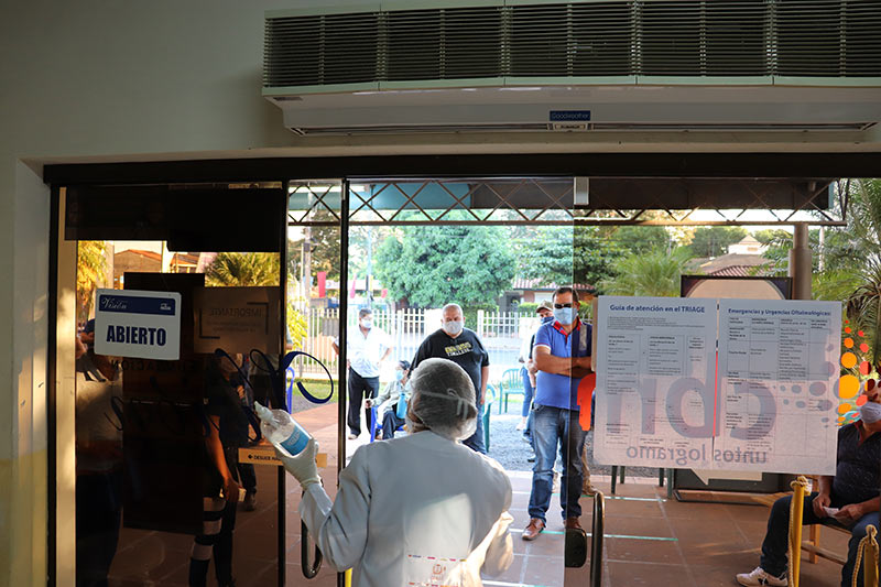 Health care worker opens door of clinic to queue of patients waiting outside