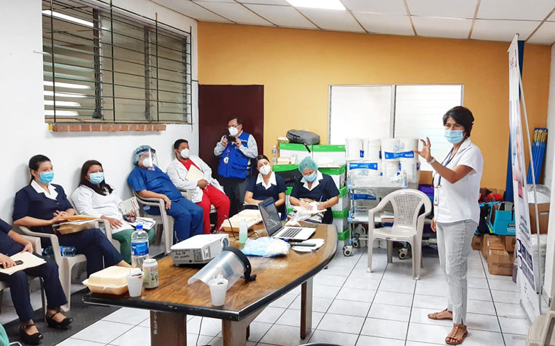 A room of hospital staff sittign down listenign to a colleague who is standing in front of them providing training