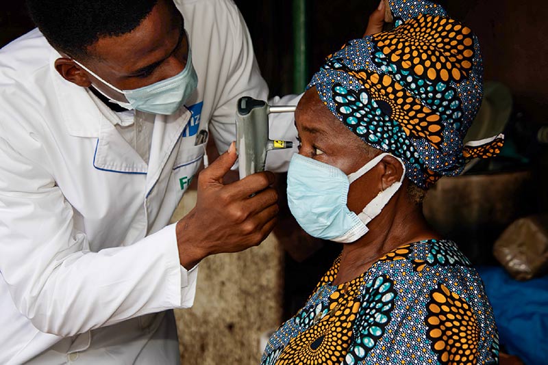 A male eye health worker holds a device up to a lady's face, to measure the intraocular pressure in her right eye