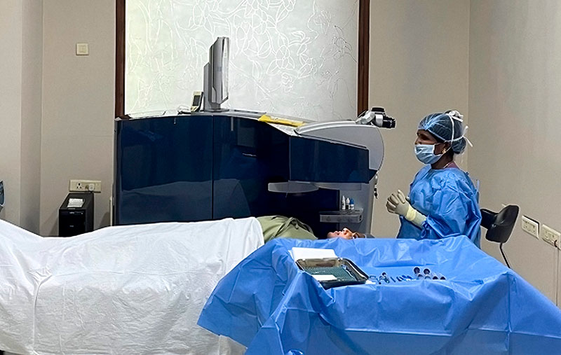 A surgeon wearing blues is sitting behind the head of the patient who is lying on a theatre bed