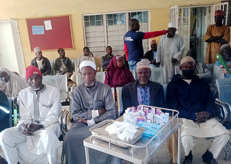Several male patients sitting down in the waiting area. In the foreground is a trolley with various items on it.