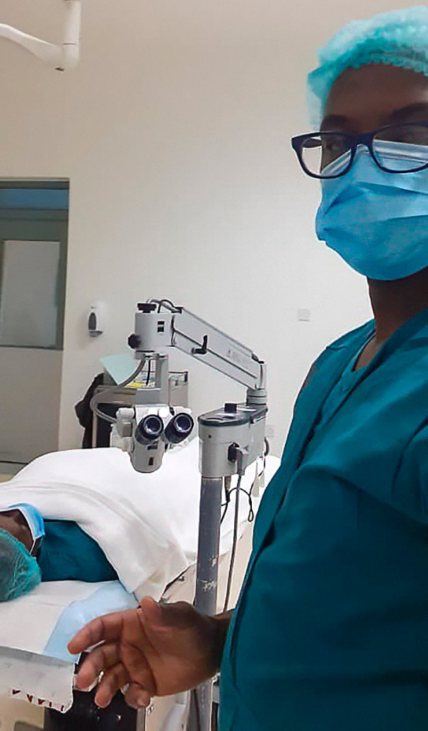 An opthalmic nurse wearing scrubs standing in and operating theatre next to a patient lying on an operating bed