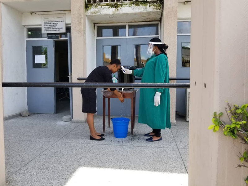 A nurse wearing green scrubs, using a handheld thermometer to check a patient's temperature prior to entry to the clinic building