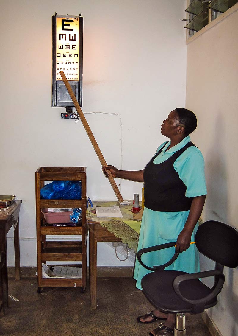 Une agente de santé se tient devant une échelle d’optotypes rétroéclairée et pointe une baguette vers une des lettres de l’échelle.
