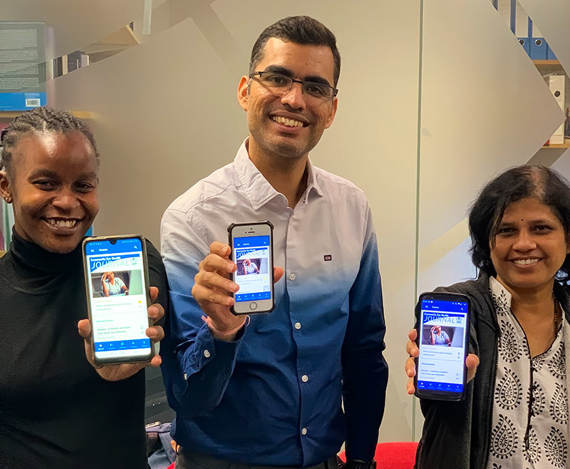 Two female and one male MSc student holding their phones towards the camera, each phone with the CEHJ App showing