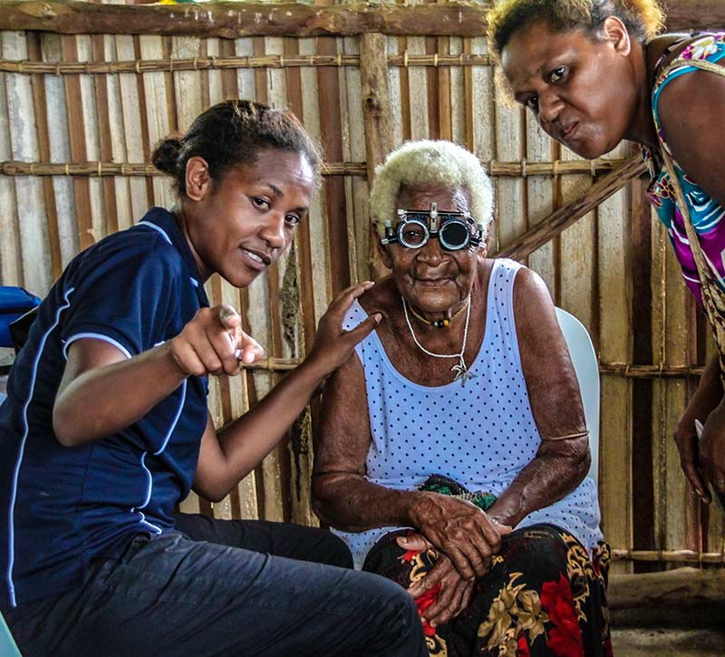 Elderly lady wearing refracting spectacles, sitting with a female optometrist who is explaining the test to her.