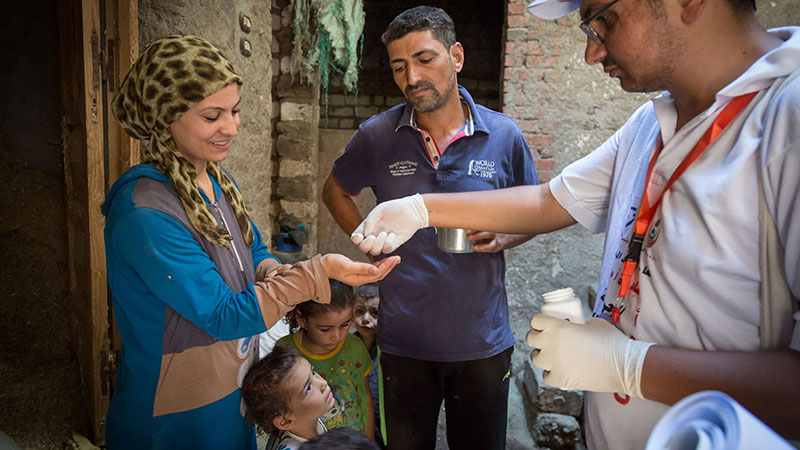 MDA to a household, man handing dose of azithromycin to a lady and her children at their front door