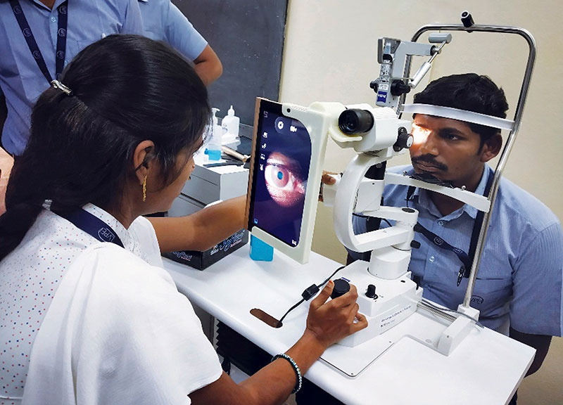 A female eye care worker takes images with a n electronic/digital tablet device which is mounted against a slit lamp, of a male patient's eye