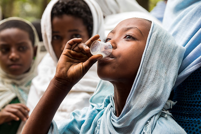 Young girl drinking azithromycin oral suspension from a clear plastic cup