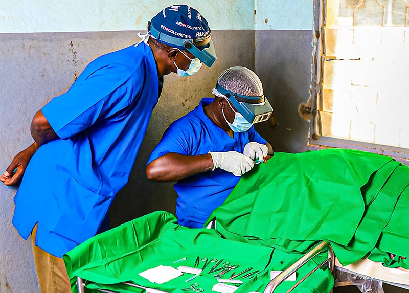 Two ophthalmic nurses in an operating room with patient draped in greens with a surgical trolley