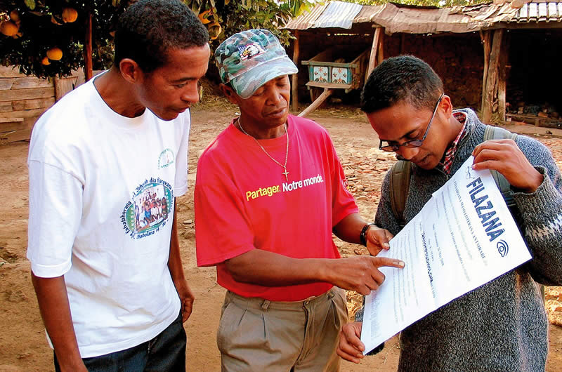Un chef de Fokontany reçoit les affichages de sensibilisation des mains de deux agents de santé oculaire communautaire. MADAGASCAR. © Henry Nkumbe