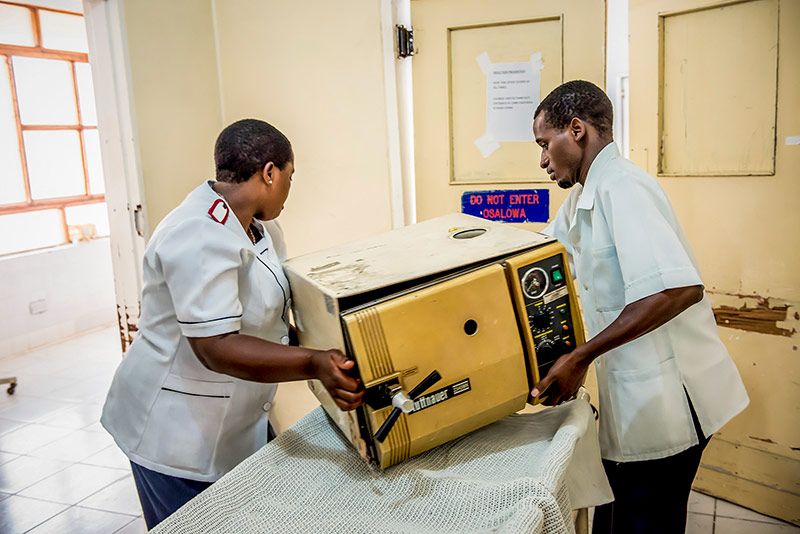 A male and a female colleague lift a heavy piece of equipment from a trolley together
