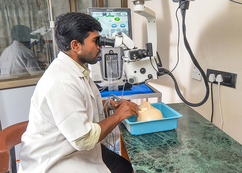 A man sits at a bench using an ophthalmic microscope